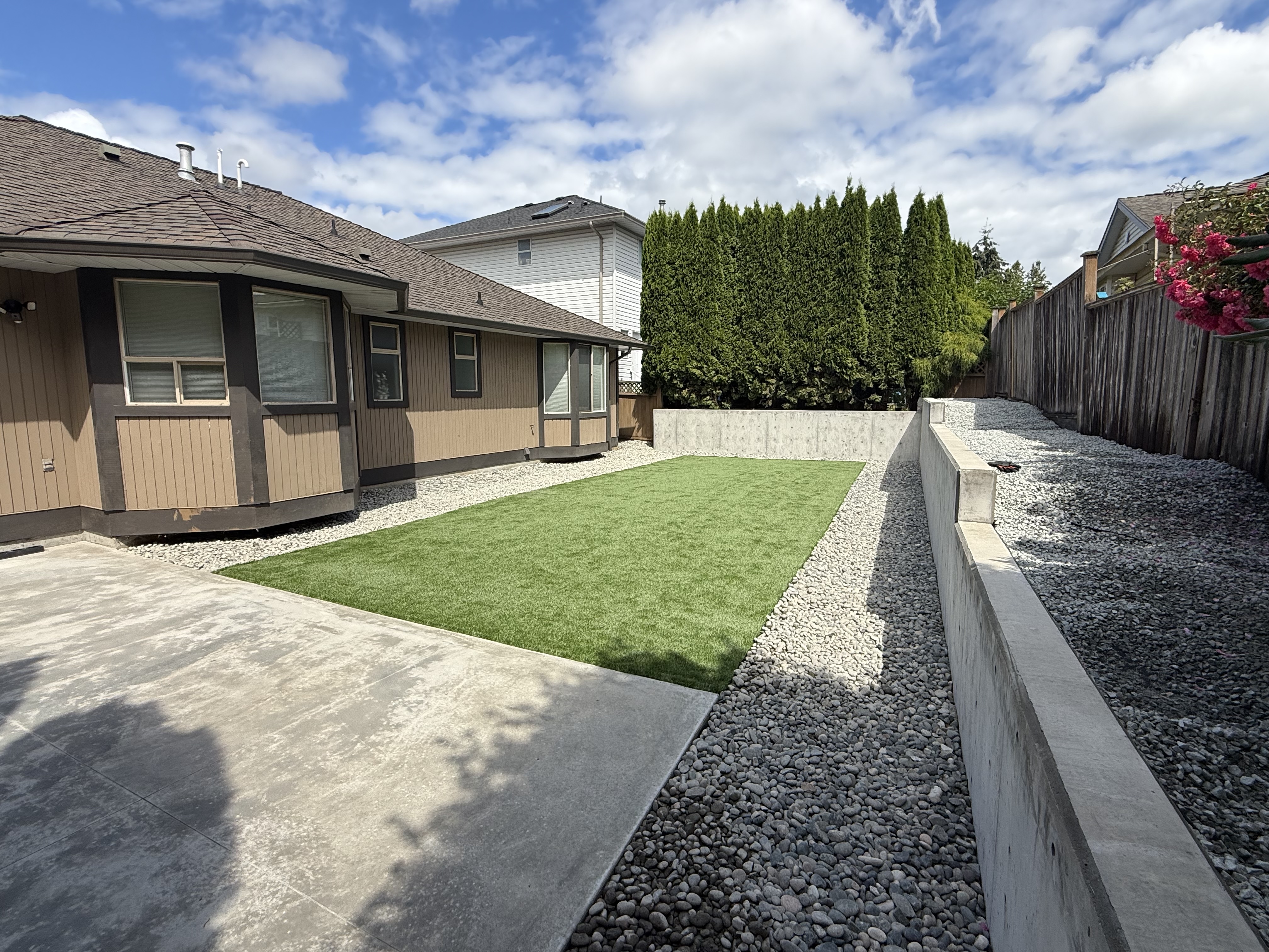 Finished concrete patio, lawn, decorative stone and concrete retaining wall beside a home
