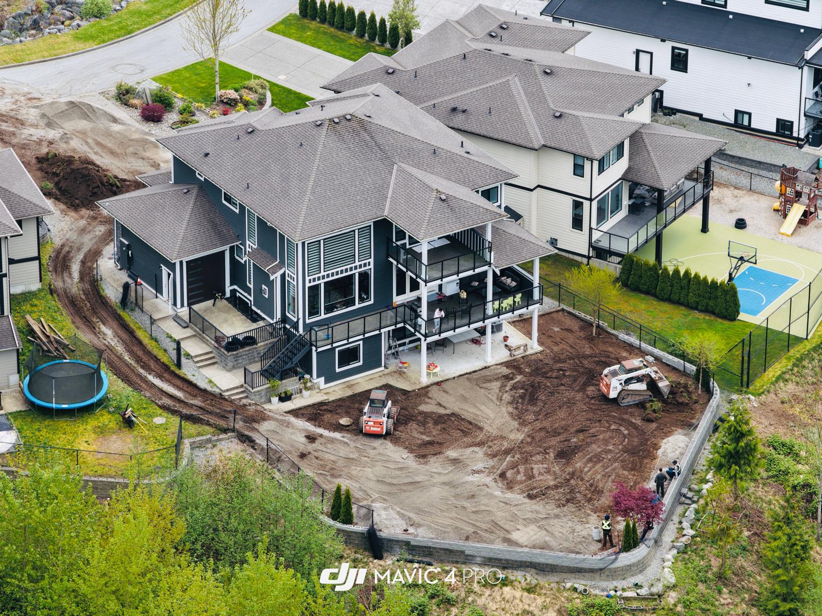 Aerial view of a large home with a curved retaining wall, grading work and two compact loaders